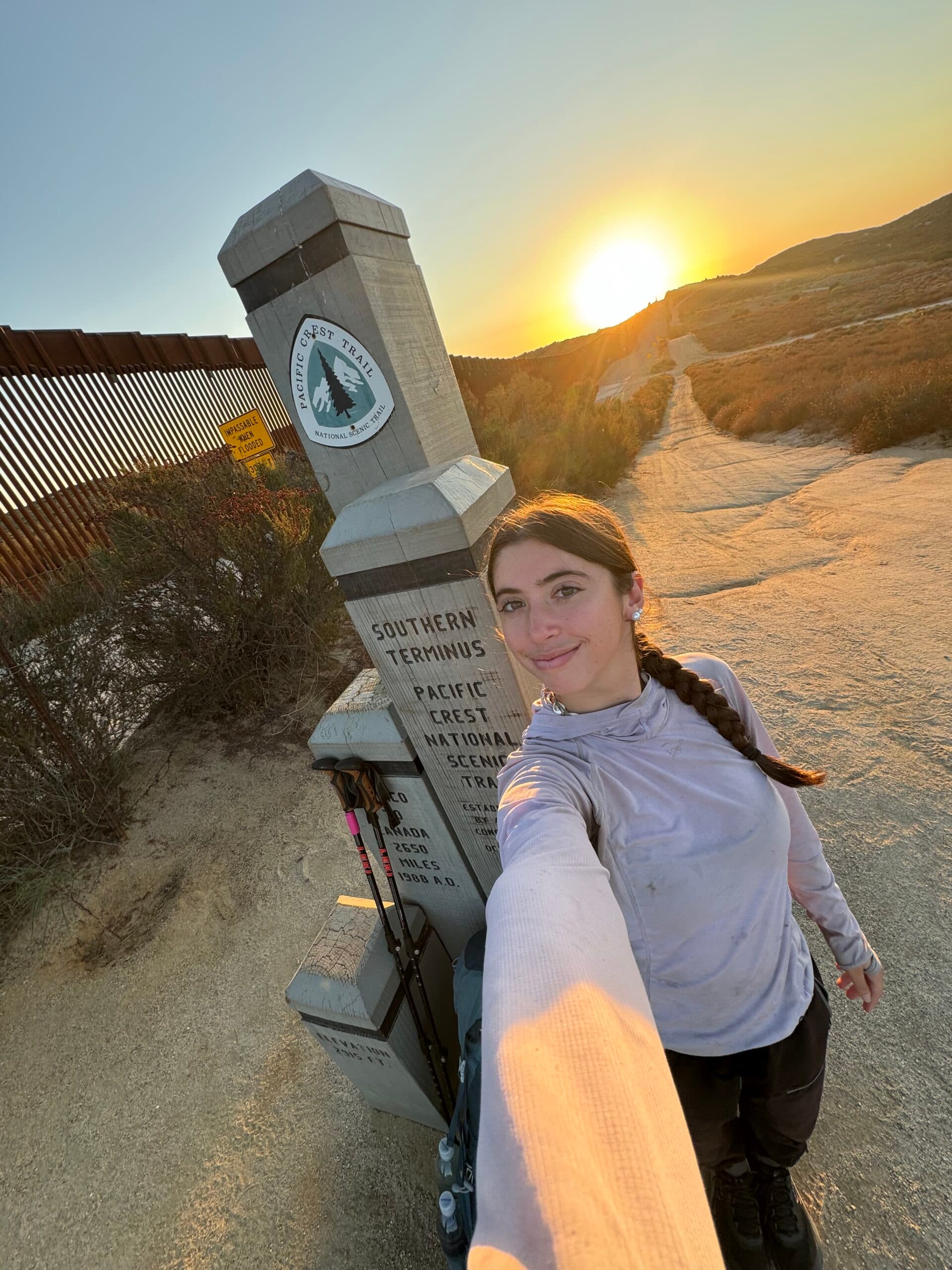 Katie Dominguez at the Pacific Crest Trail Southern Terminus at sunrise, holding hiking poles